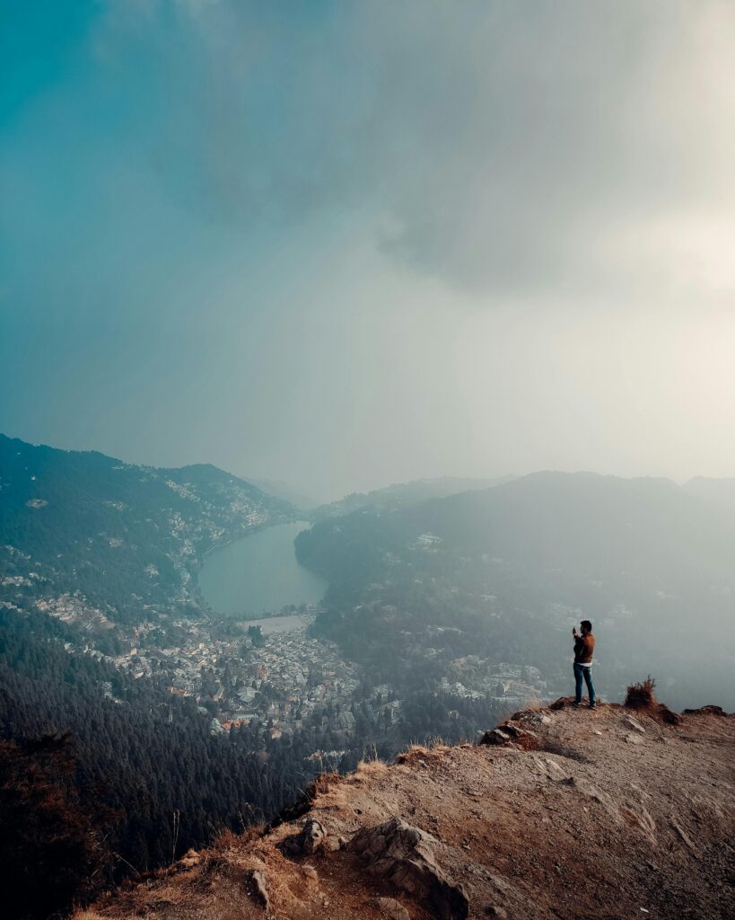 pexels-photo-7715813-7715813 A breathtaking view of Nainital Lake and mountains with a lone hiker overlooking the valley from a peak.